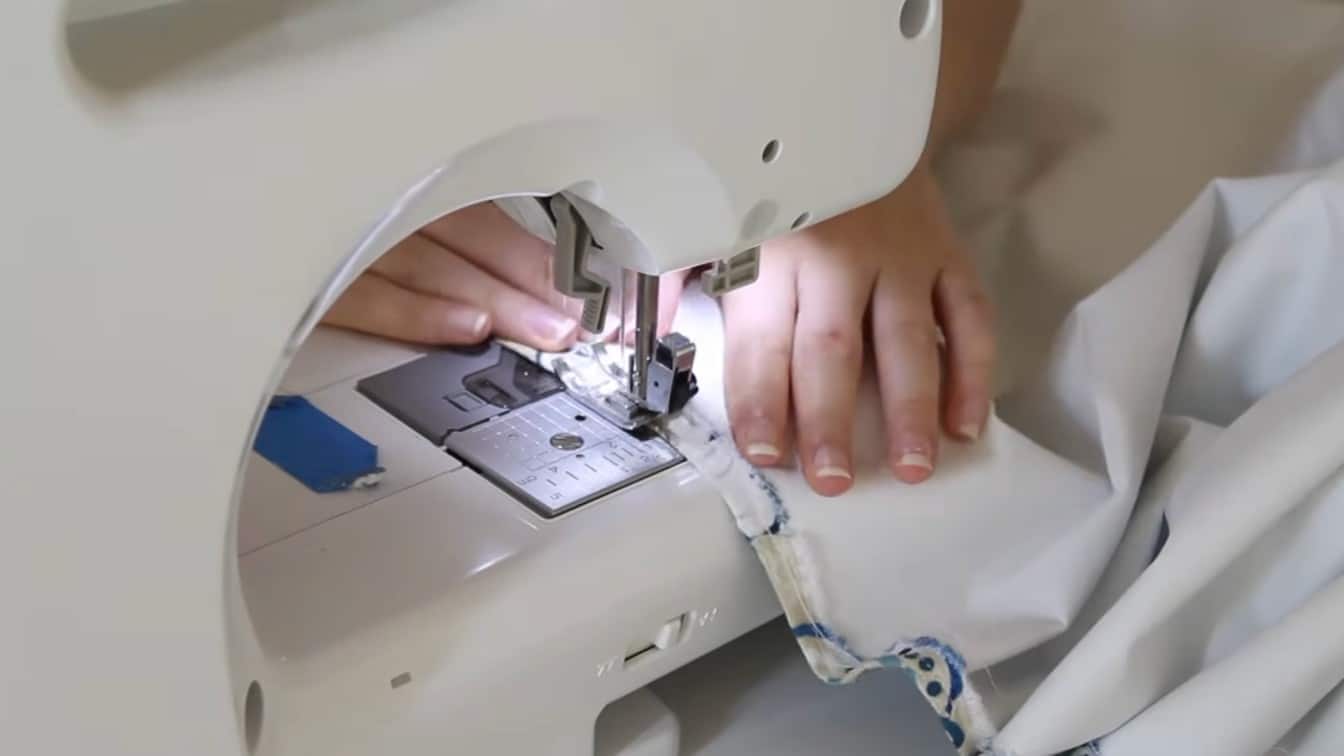 sewing machine stitching white lining fabric for a diy roman shade in a bright craft workspace