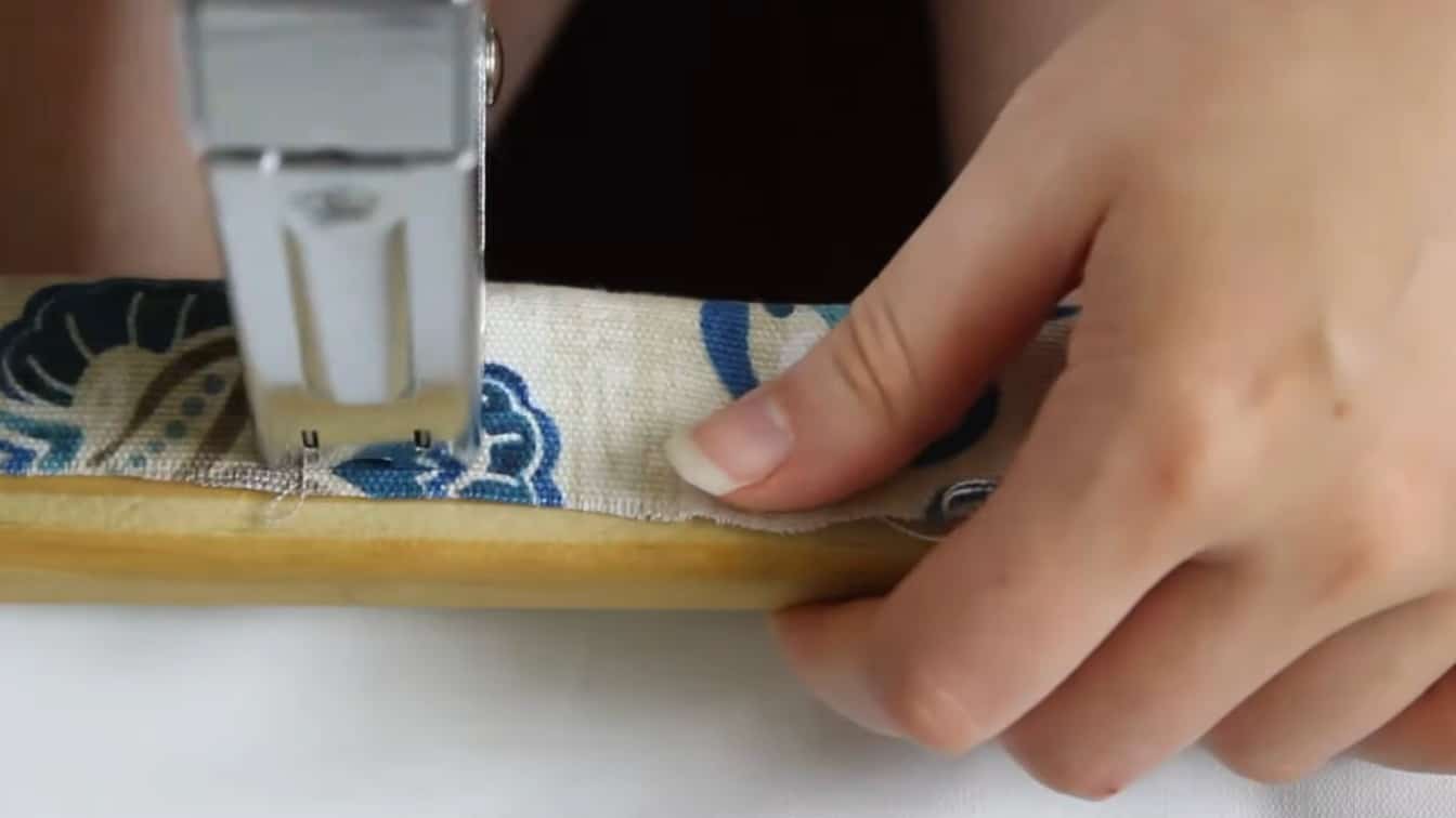 staple gun securing patterned fabric to a wood strip for a diy roman shade mounting step at home