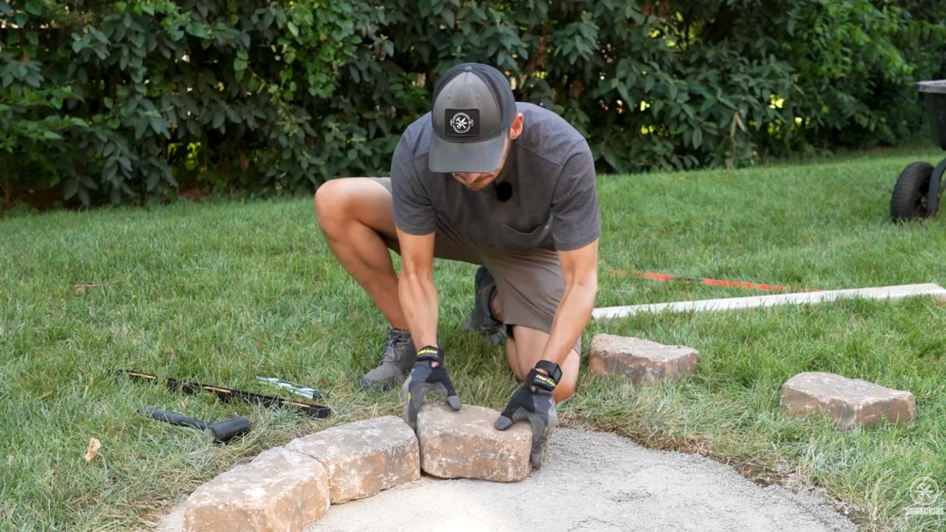 diy backyard ideas showing stone blocks being cut and adjusted for a clean round fire pit shape on grass