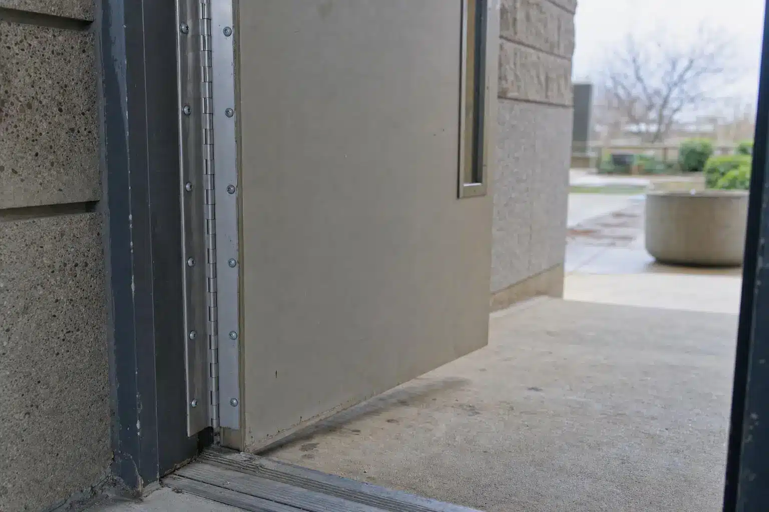 Partially open metal door leading outside to a concrete patio with planters