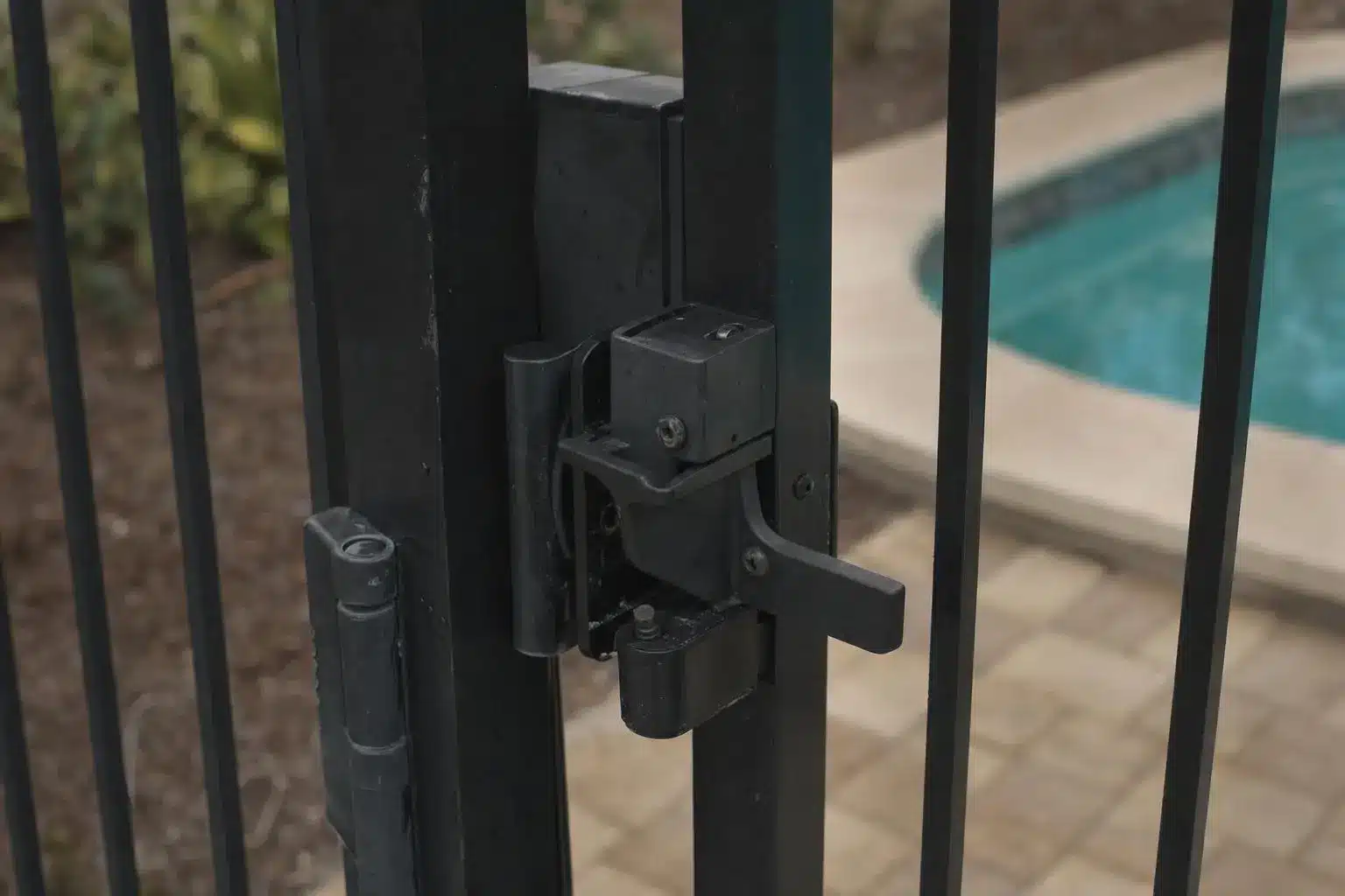 Iron gate latch with pool in background and stone patio setting