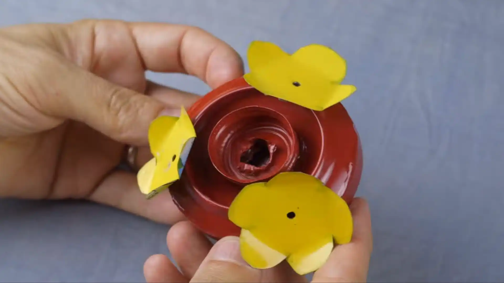 hands holding a red metal craft with three yellow flower-shaped blades attached around the center hole