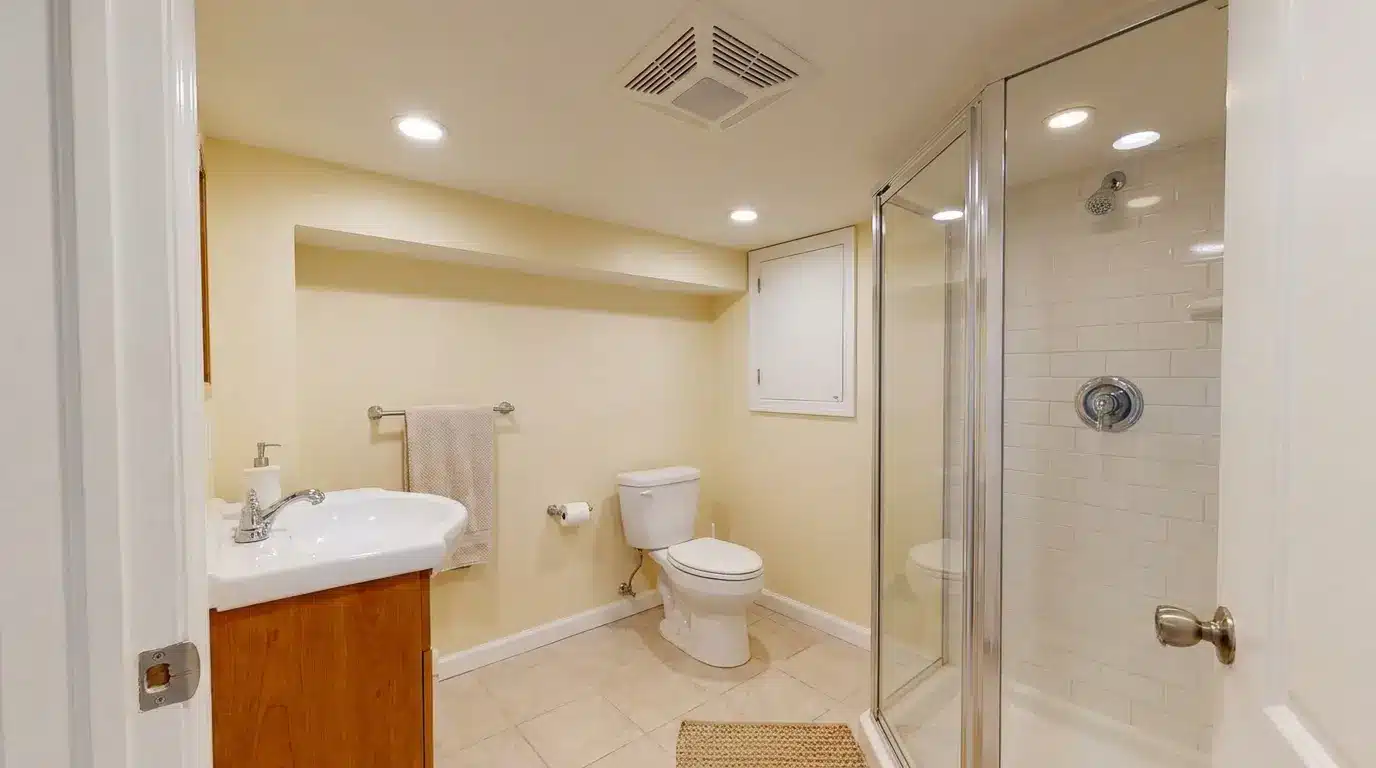 basement bathroom with compact shower toilet vanity ventilation and bright lower level lighting