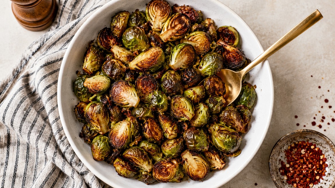 winter vegetables crispy brussels sprouts in a white bowl with golden spoon and warm striped kitchen towel