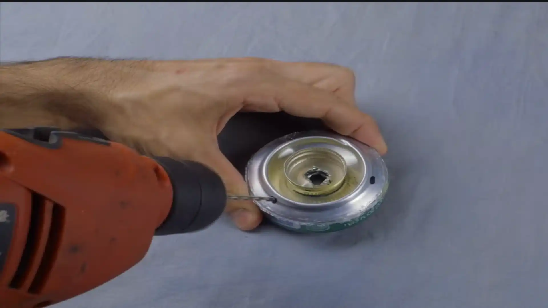 hand using a power drill to make a hole in a modified beverage can with a bottle cap attached