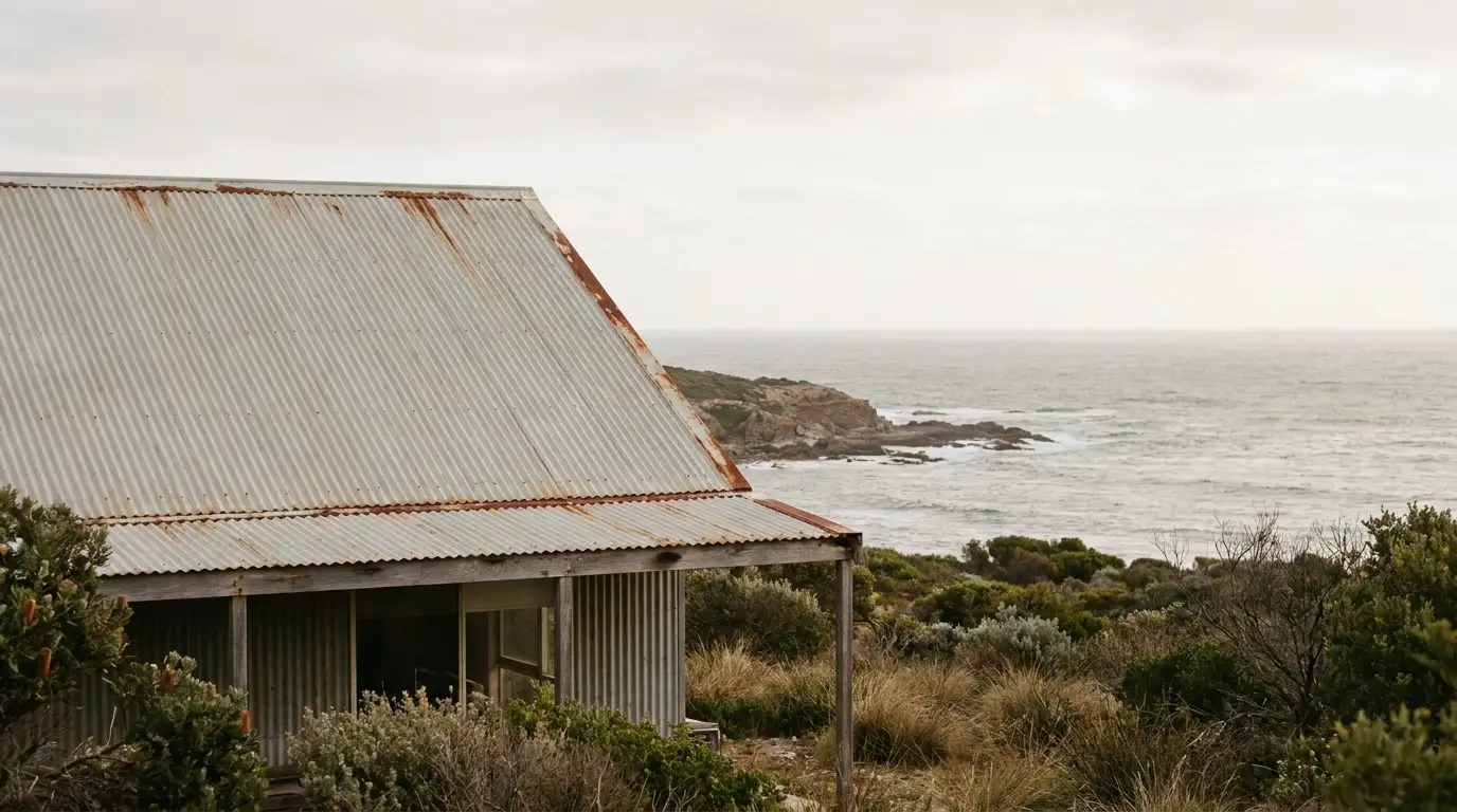 Rustic corrugated metal shed overlooking ocean with rugged coastline and coastal vegetation