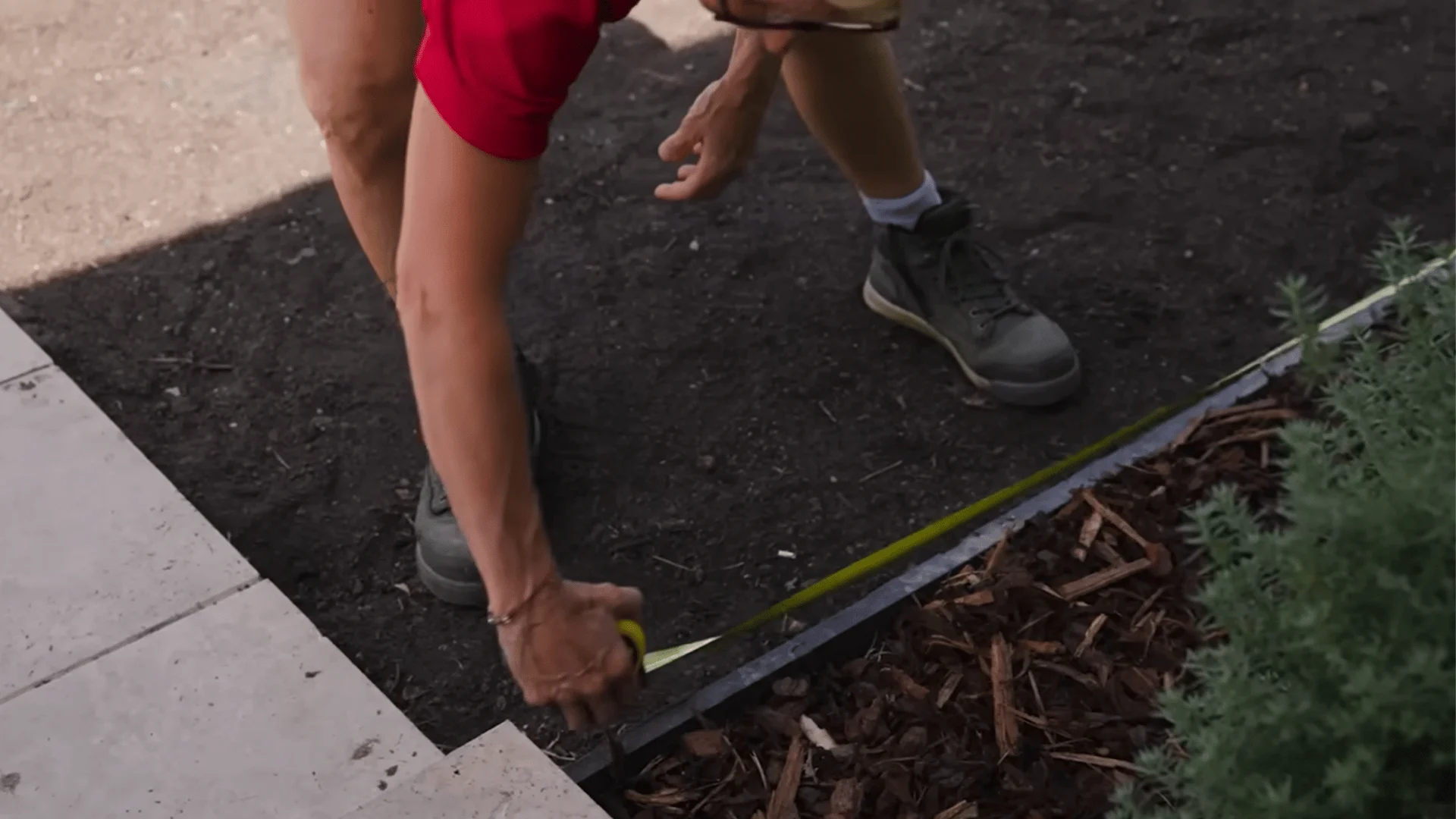 person measuring the edge of a prepared lawn area with a tape measure before calculating seed needs