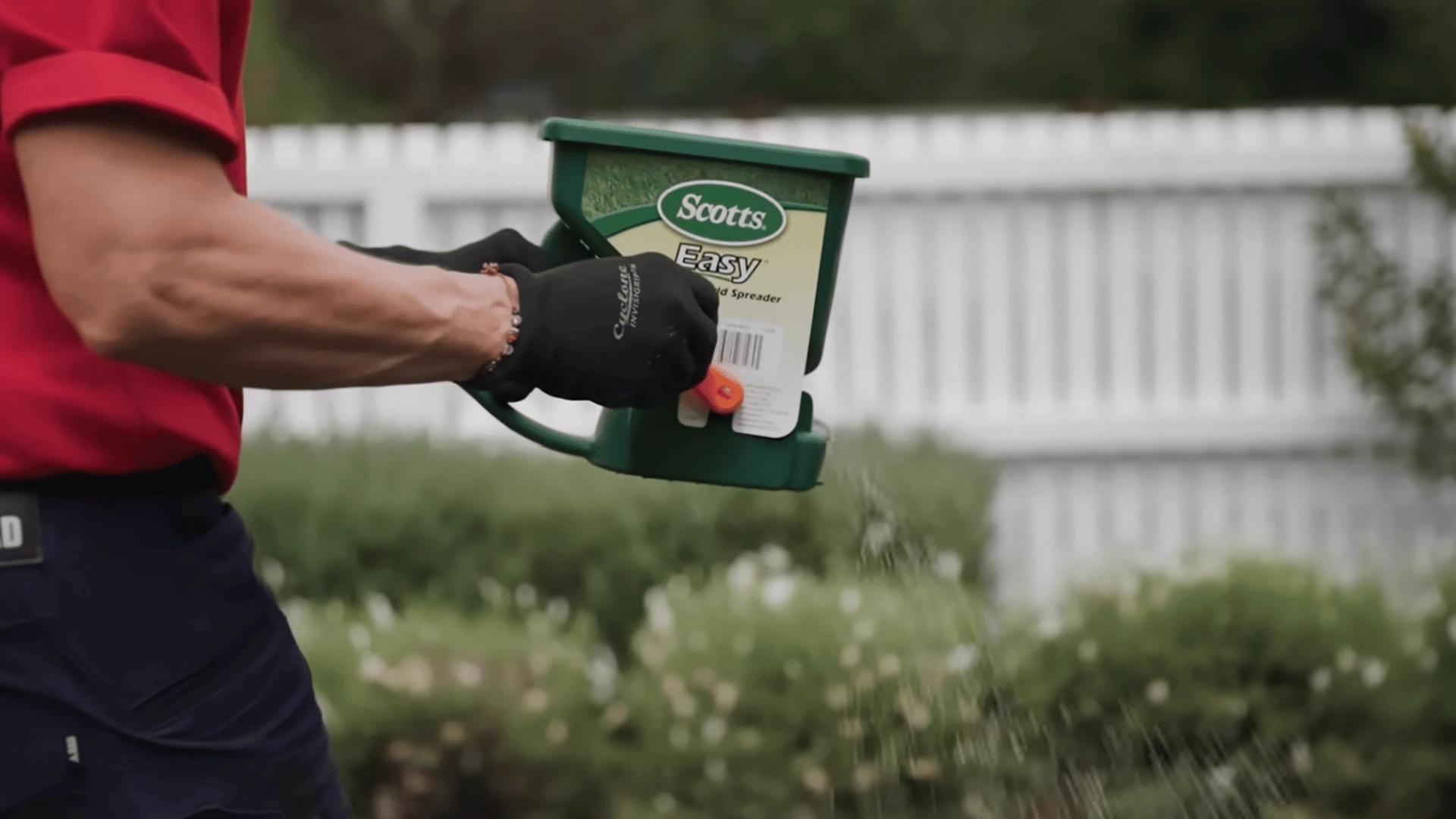 person using a handheld spreader to apply grass seed evenly across a prepared backyard lawn area