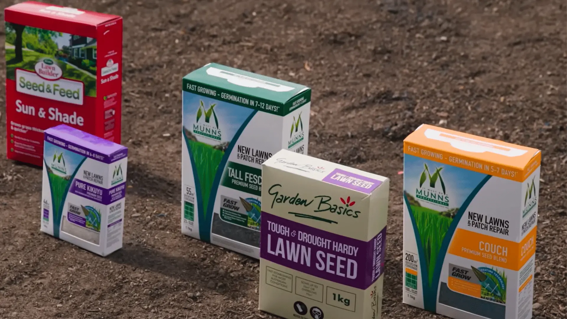 several grass seed boxes placed on bare soil showing different seed types for lawns and patch repair