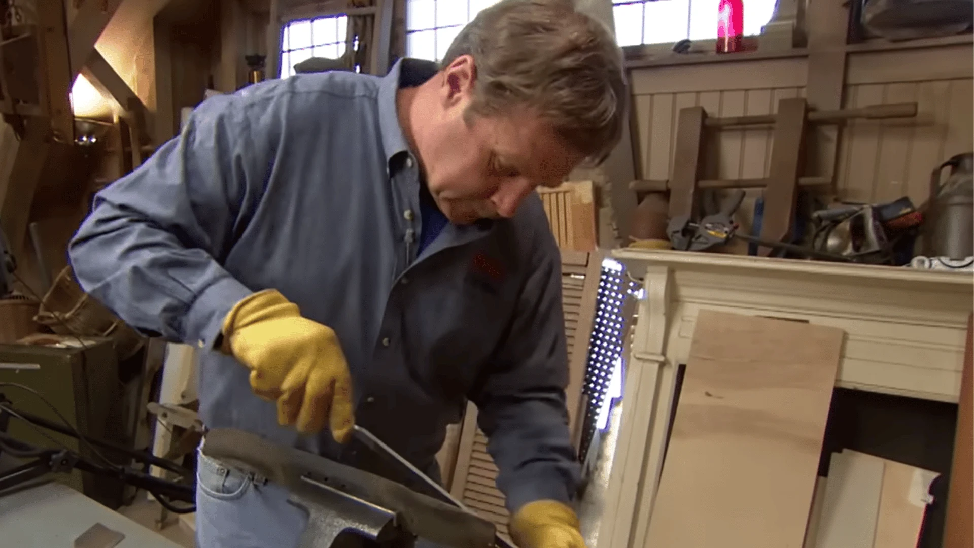 gloved man sharpens a lawn mower blade with an angle grinder while the blade rests in a bench vise