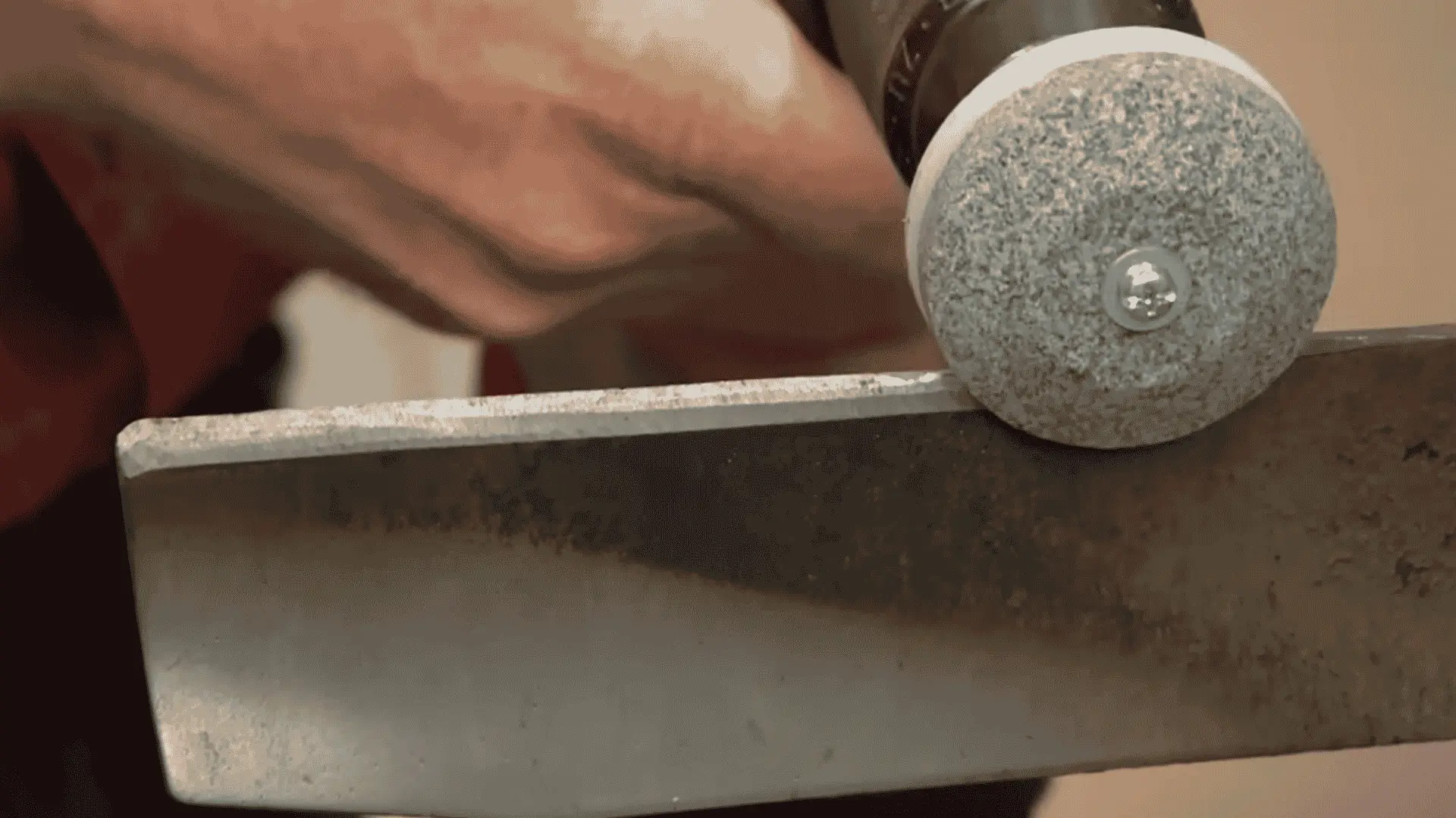 close-up of a drill-mounted sharpening stone restoring the cutting edge of a lawn mower blade