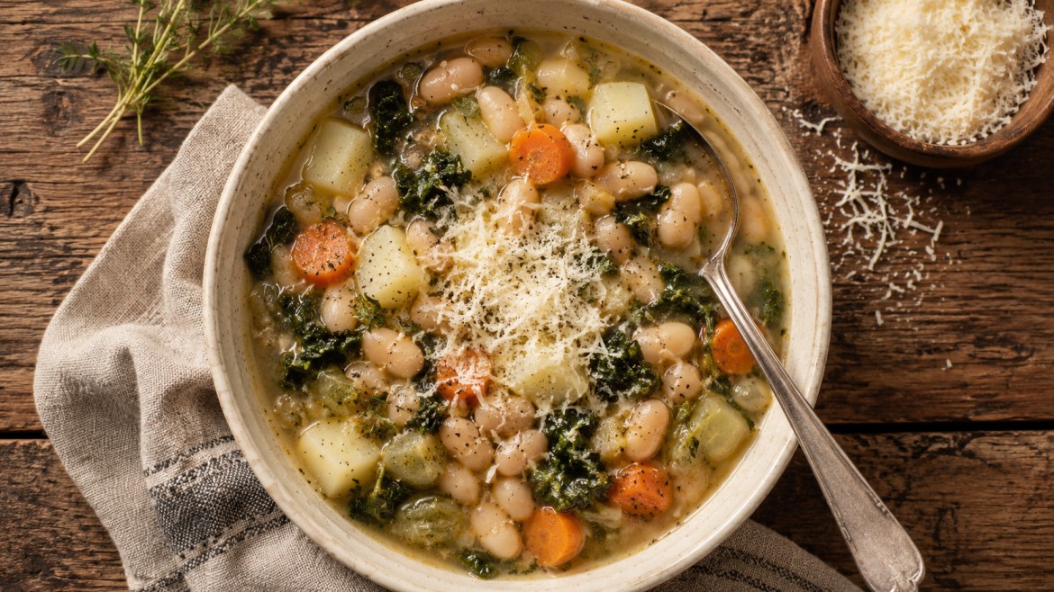winter vegetables white bean potato soup with carrots kale grated cheese and spoon on rustic wood table