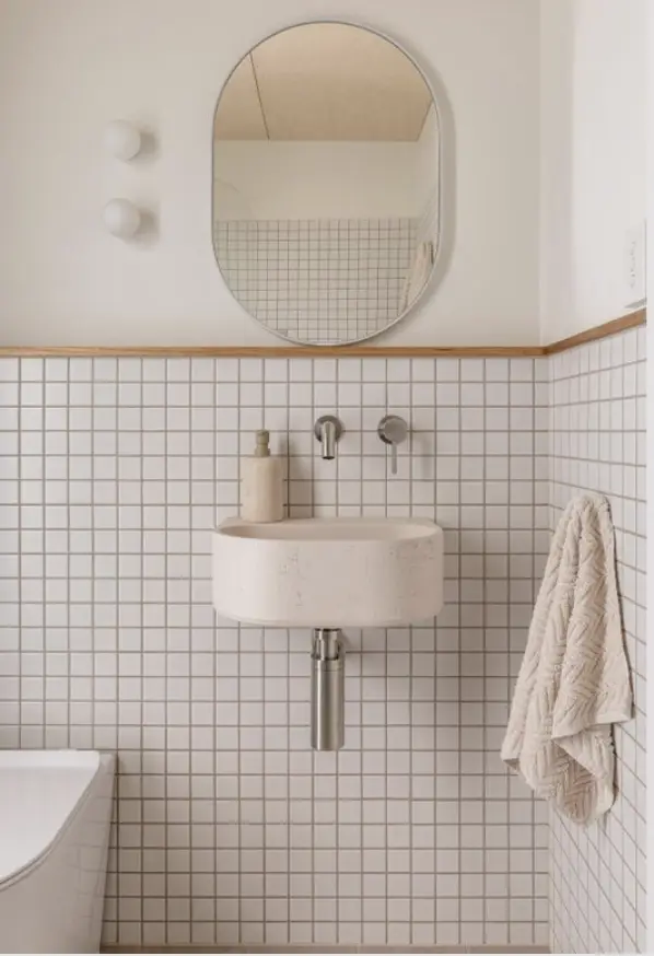 Modern bathroom with wall-mounted sink, round mirror, and textured towel against white tiled wall