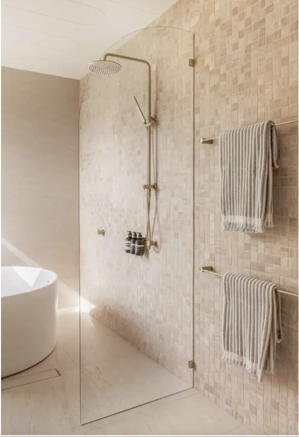 Modern bathroom with glass shower, beige mosaic tiles, round bathtub, and striped towels on rails