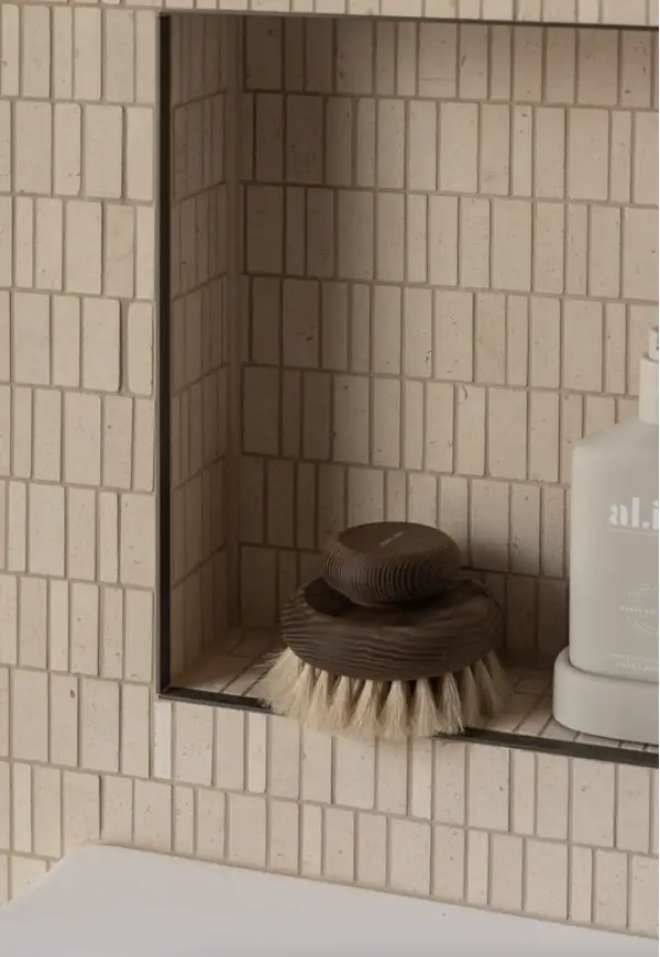Wooden bath brush and bottle on tiled shelf in neutral bathroom setting