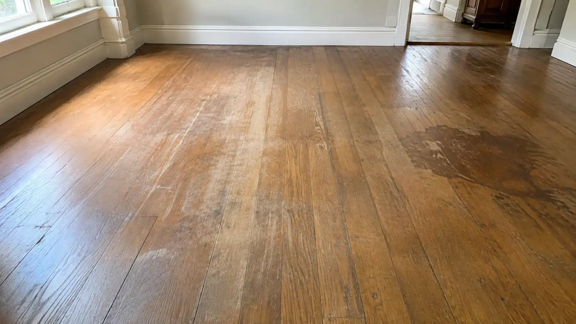 worn hardwood floor with scratches faded finish and uneven patches showing clear signs of age and damage